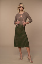 Woman wearing an olive and pink  marled pattern cardigan  and green skirt with pink dots against a beige background