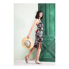 Anna Bird Jacquard Skirt in Black - VIAVAI FASHION  Photograph of a brunette girl with bangs modeling a V neck strap top and  below the knee pencil skirt in black color with a bird , floral, and fruit pattern  in grey, yellow, blue and purple colors. Photo of side view showing the slit while she is walking in kitten heels and holding a  straw hat 